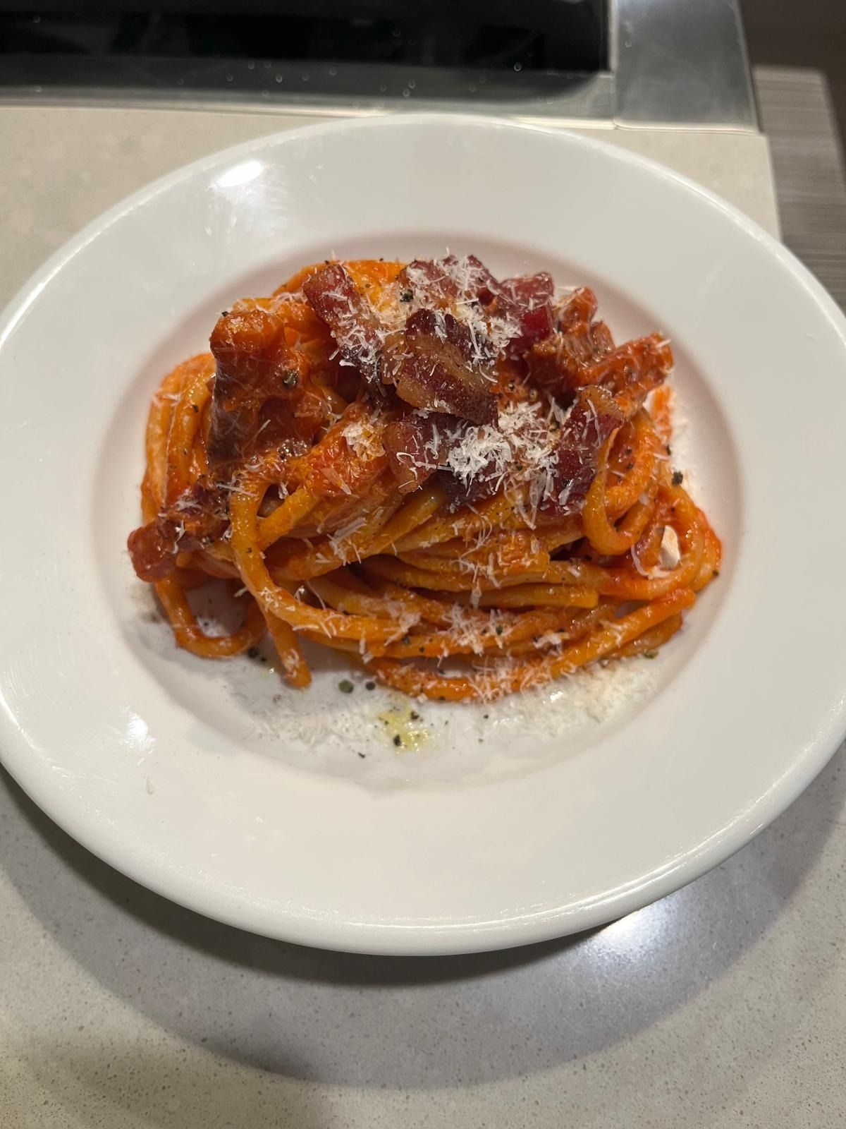 A nest of pasta all'amatriciana topped with crisp pieces of guanciale and grated cheese, on a white plate