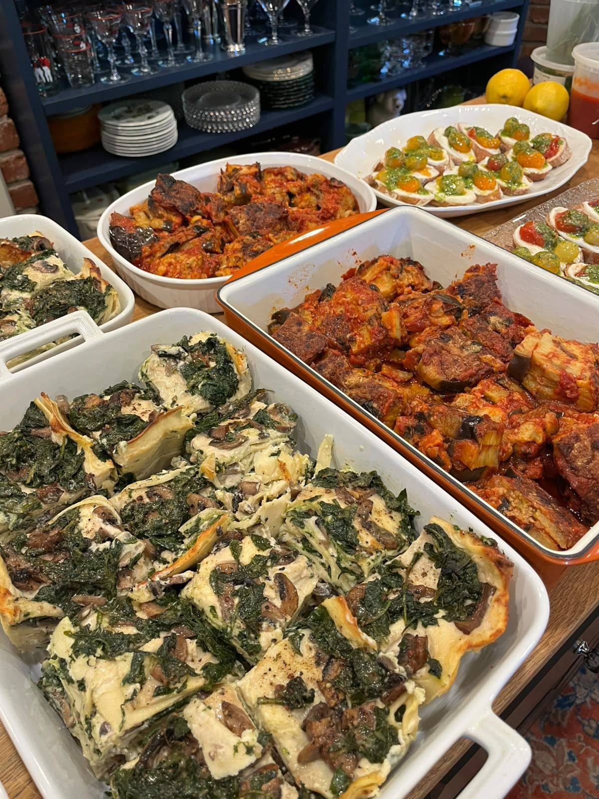 The buffet at the birthday for 24, with baking dishes of white lasagna with spinach and mushrooms, more dishes and a tray of crostini behind