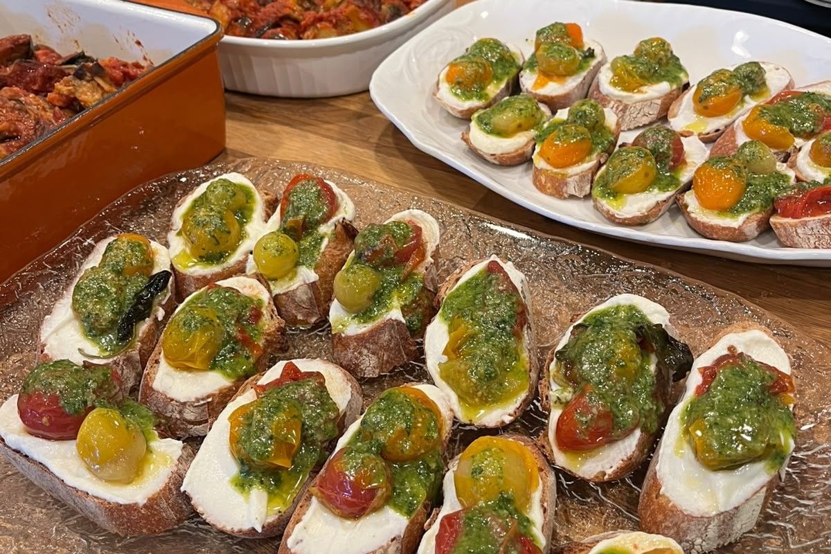 Crostini with whipped ricotta, confit cherry tomatoes and pesto on a glass platter, at the birthday buffet