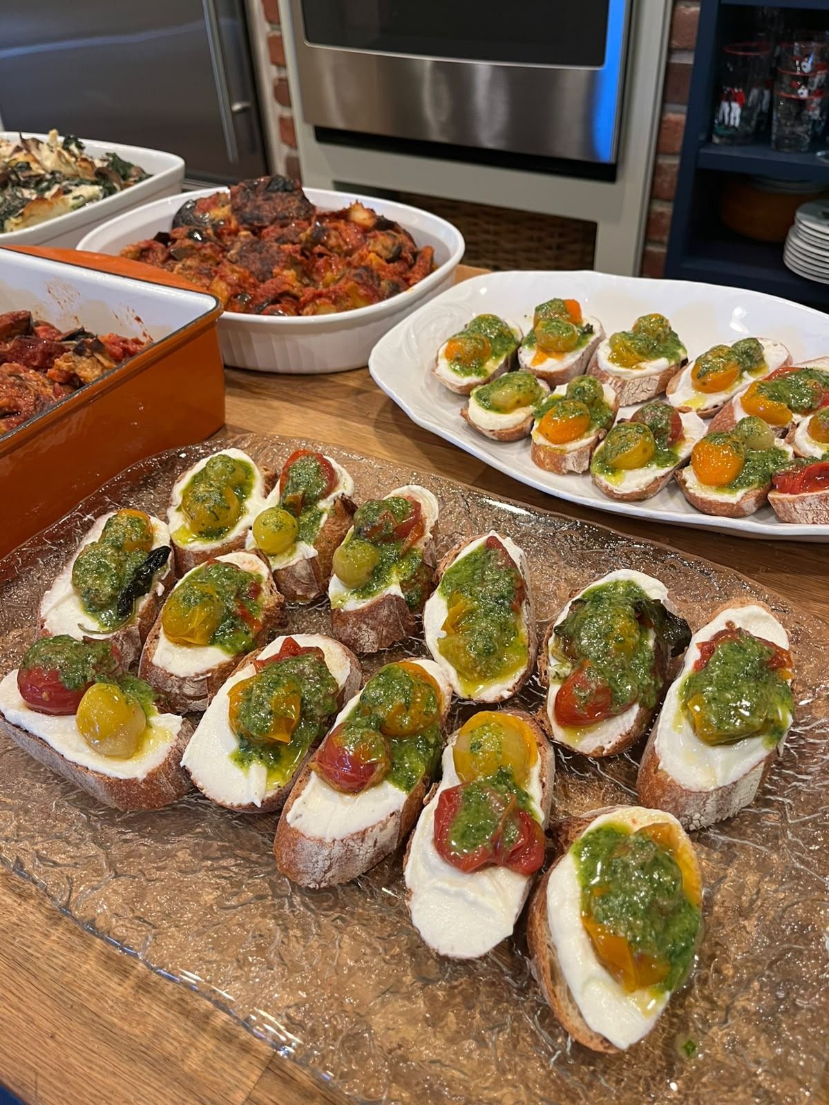 Crostini with whipped ricotta, confit cherry tomatoes and pesto on a glass platter