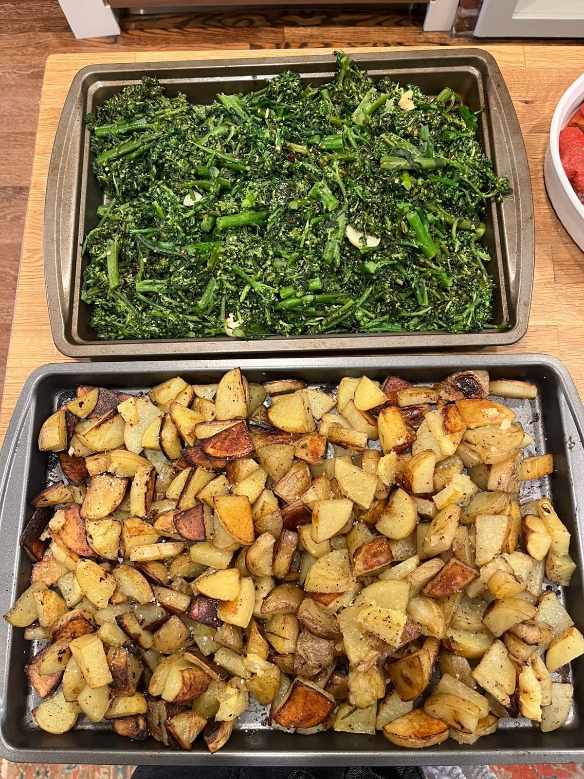 A tray of broccolini sautéed with garlic, above a tray of roast potatoes