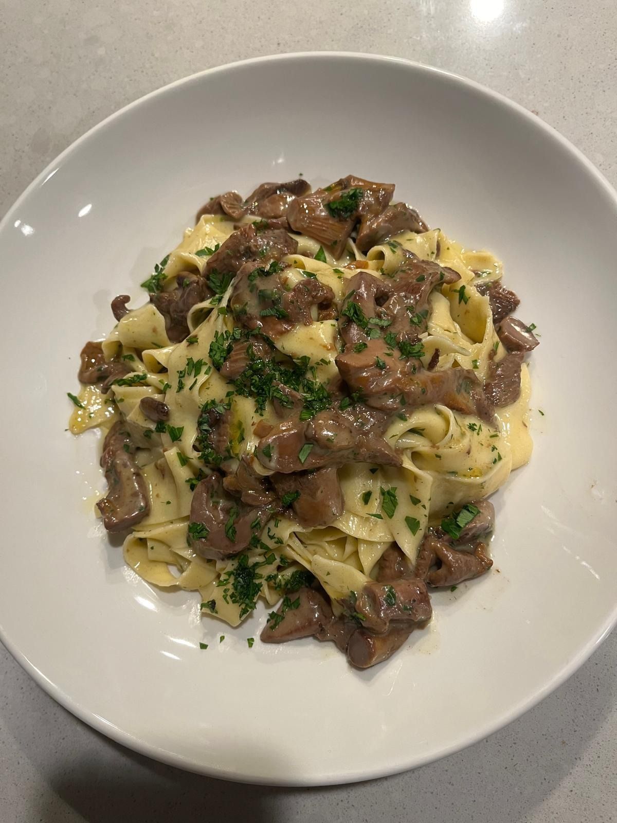 Fettuccine with sliced mushrooms and chopped parsley in a wide white bowl, seen from above