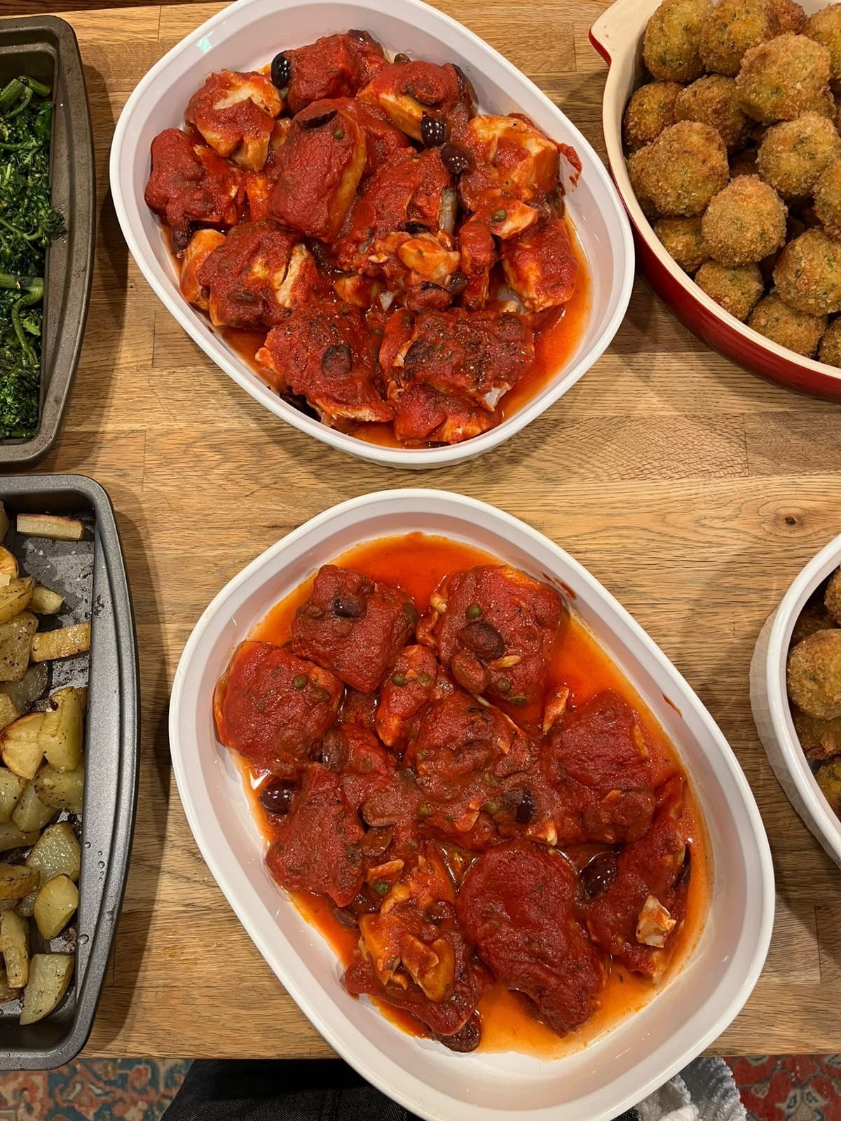 Cod in tomato sauce with olives and capers in white baking dishes, next to a dish of fried fish croquettes