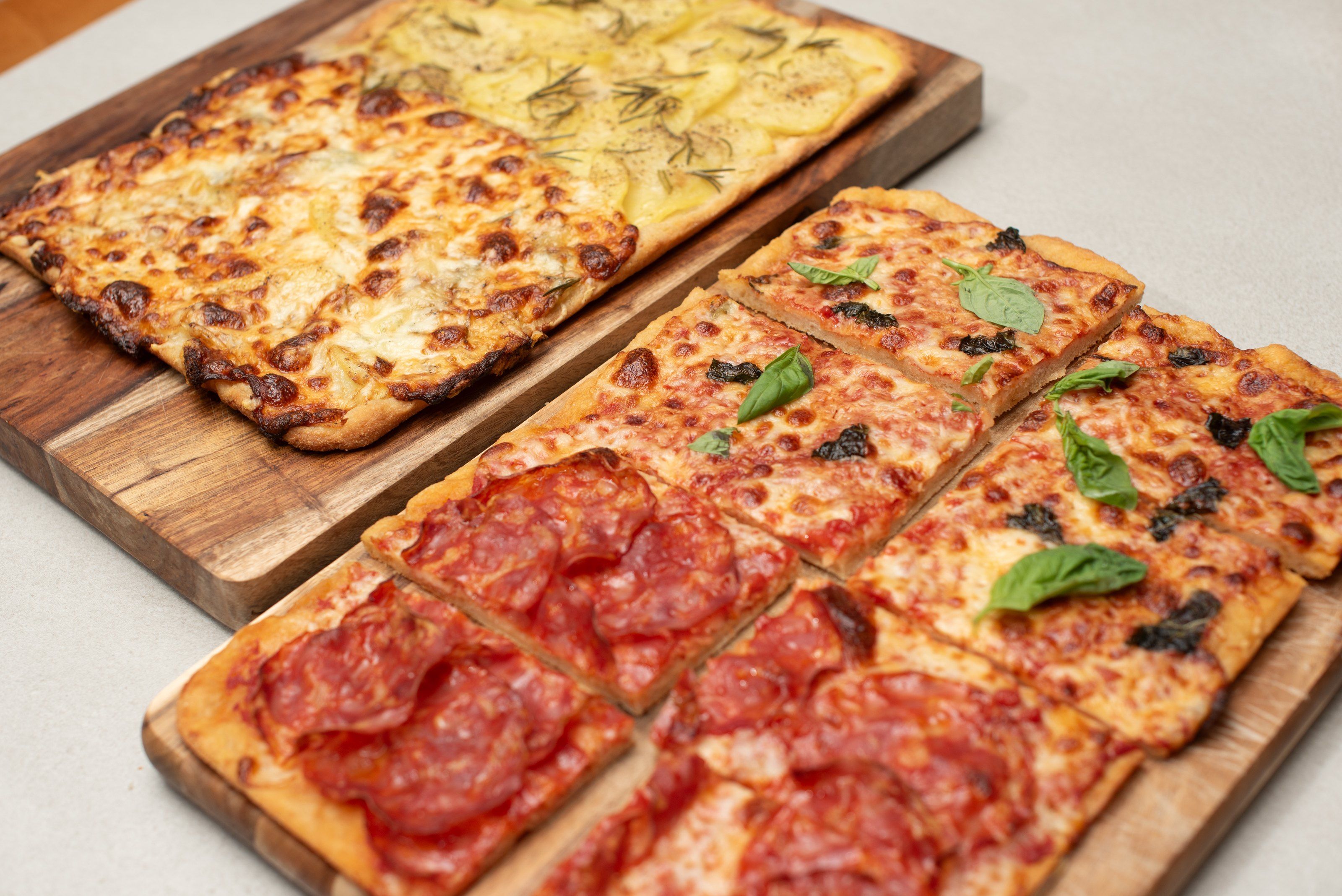 Roman pizza al taglio on two wooden boards, with salami and basil on one and potato with rosemary on the other