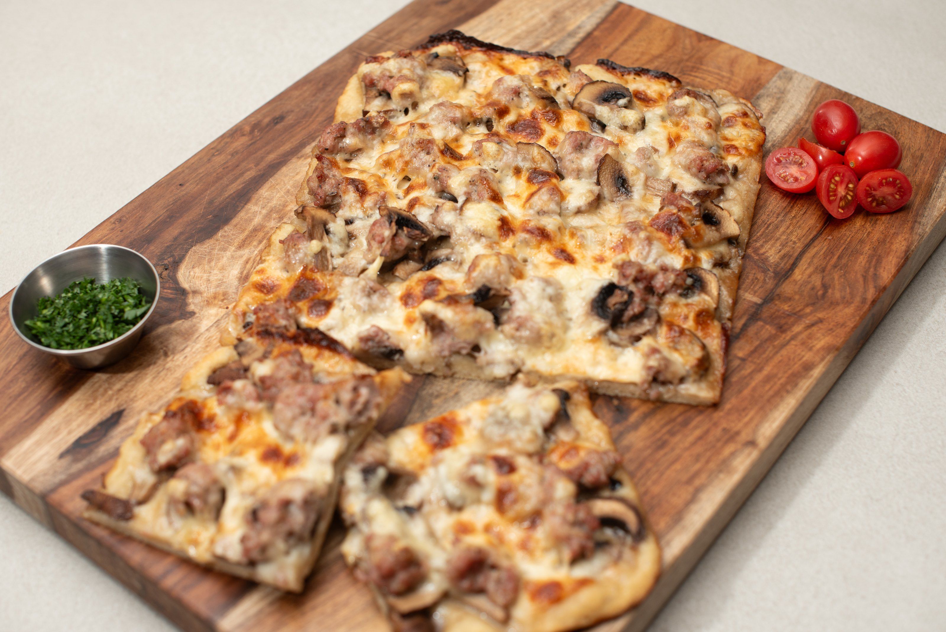 Pizza al taglio with sausage and mushroom on a wooden board, with cherry tomatoes and parsley
