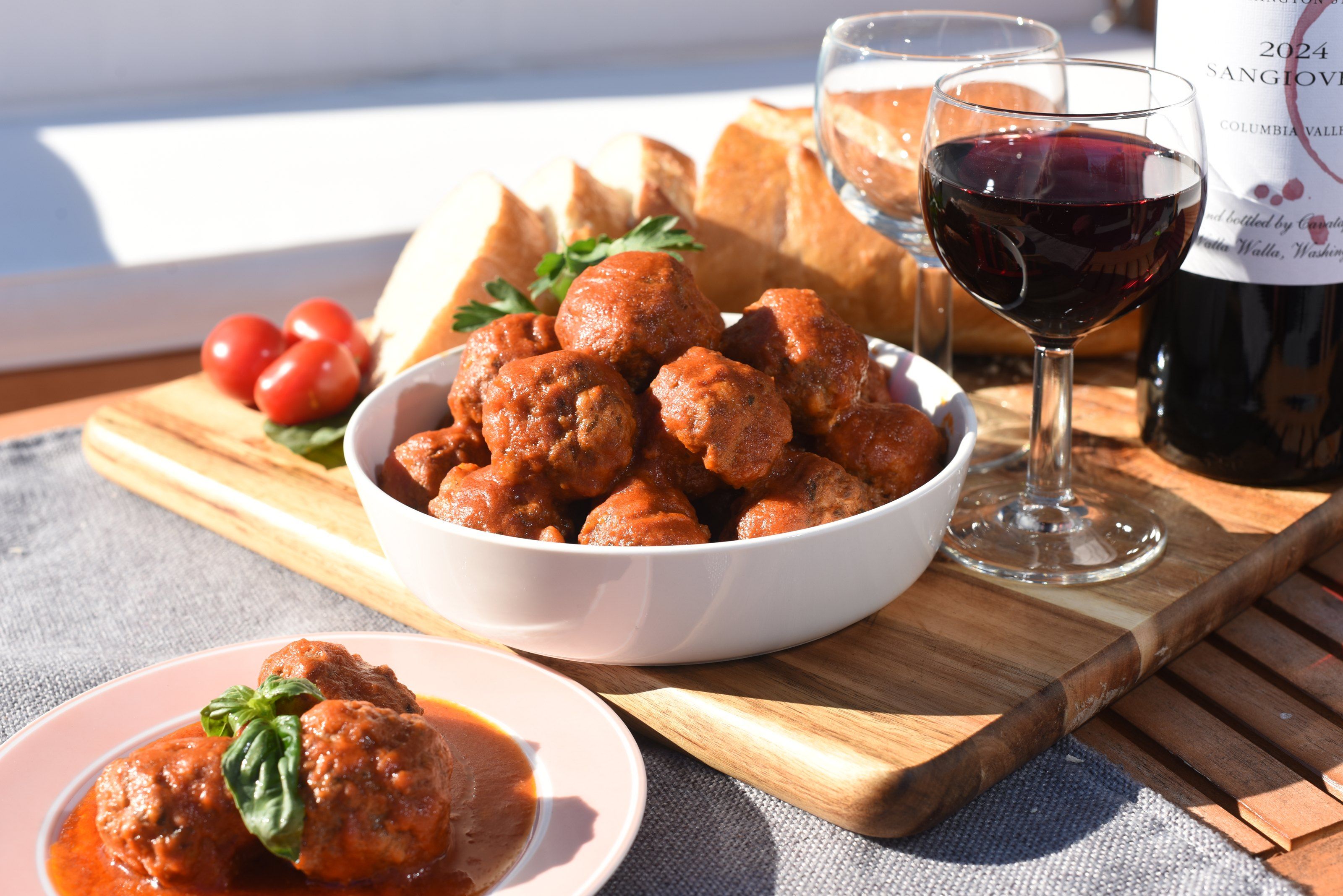 Meatballs in tomato sauce in a white bowl, with red wine and bread