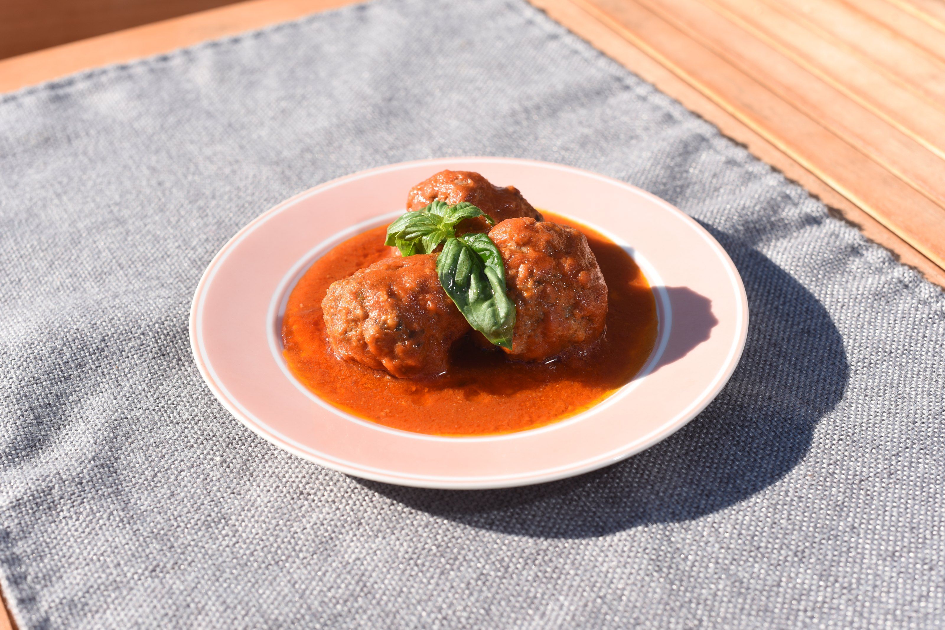 Two meatballs in tomato sauce with basil on a pink plate