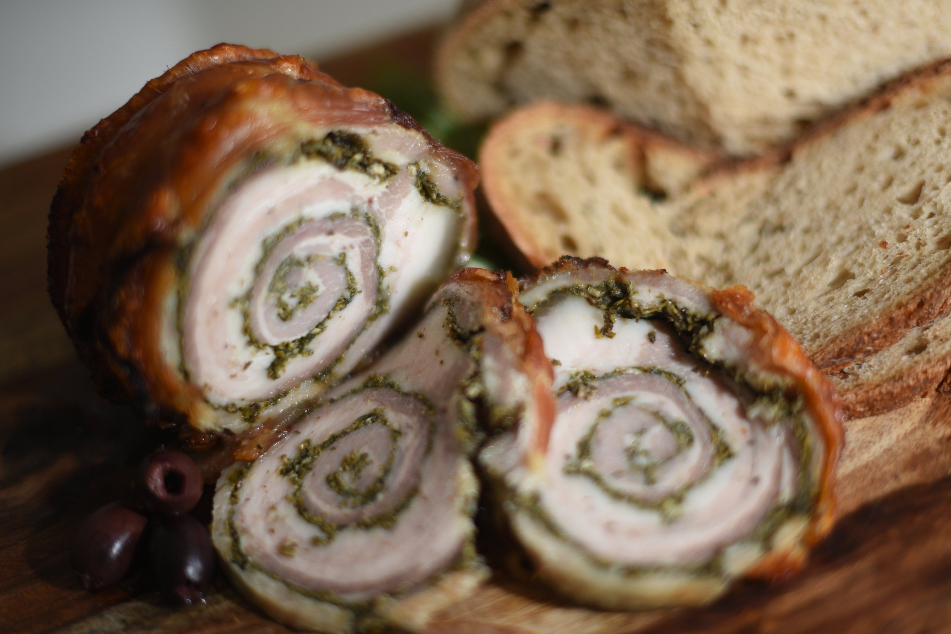Close-up of porchetta slices with black olives and country bread