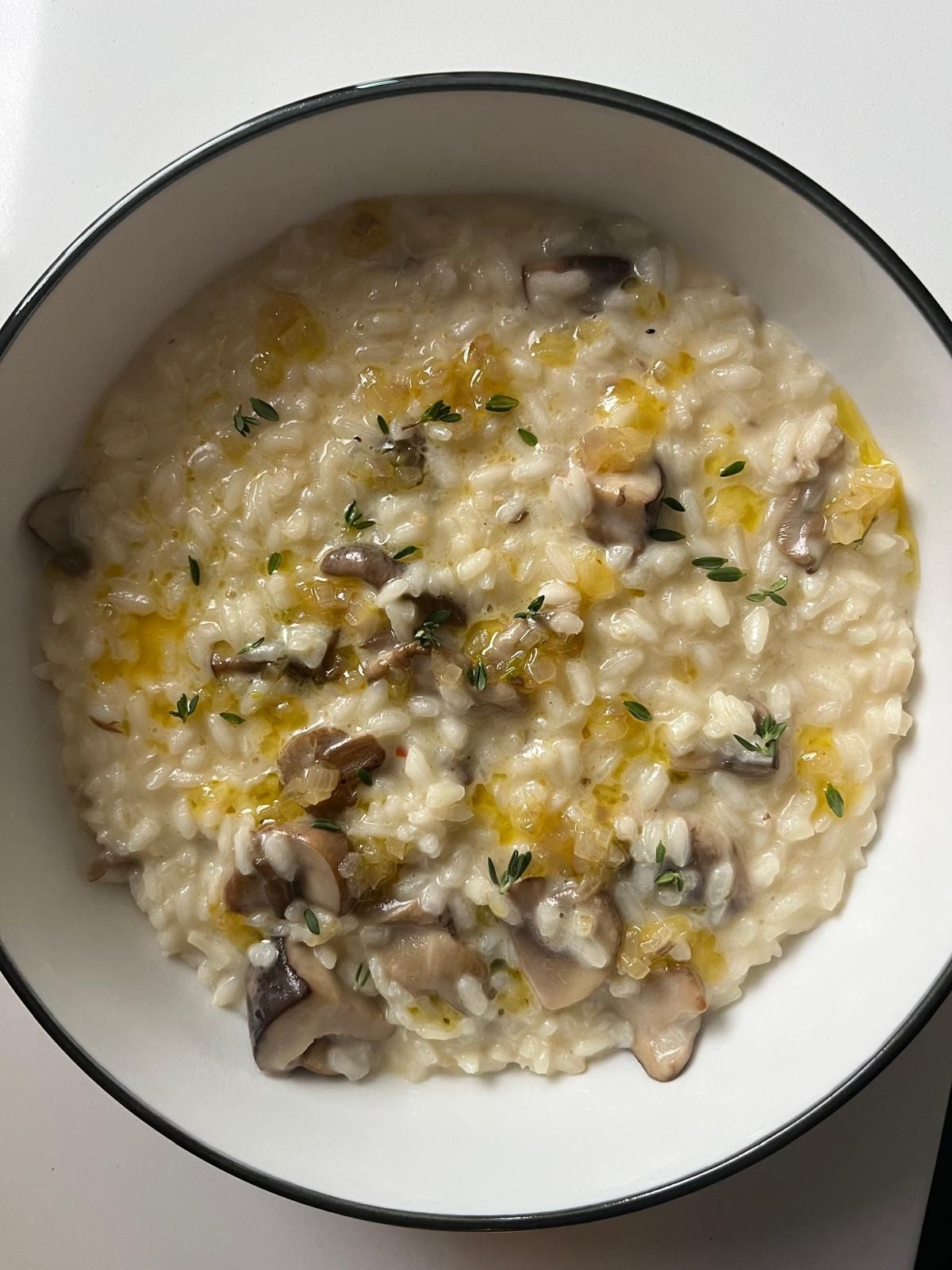 Mushroom risotto with thyme leaves and a drizzle of oil in a white bowl with a dark rim