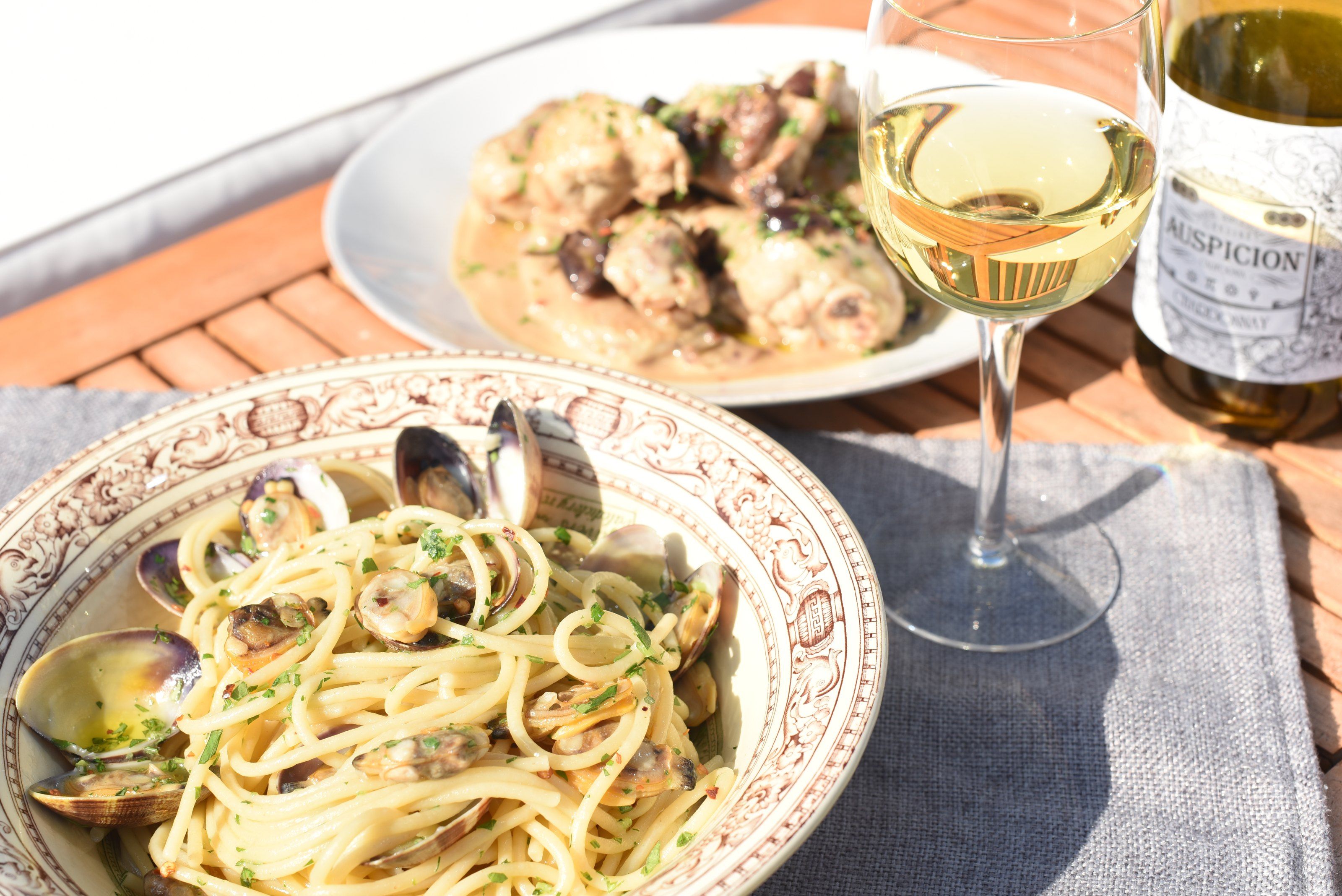 Spaghetti with clams and chicken cacciatora on a sunny table with white wine