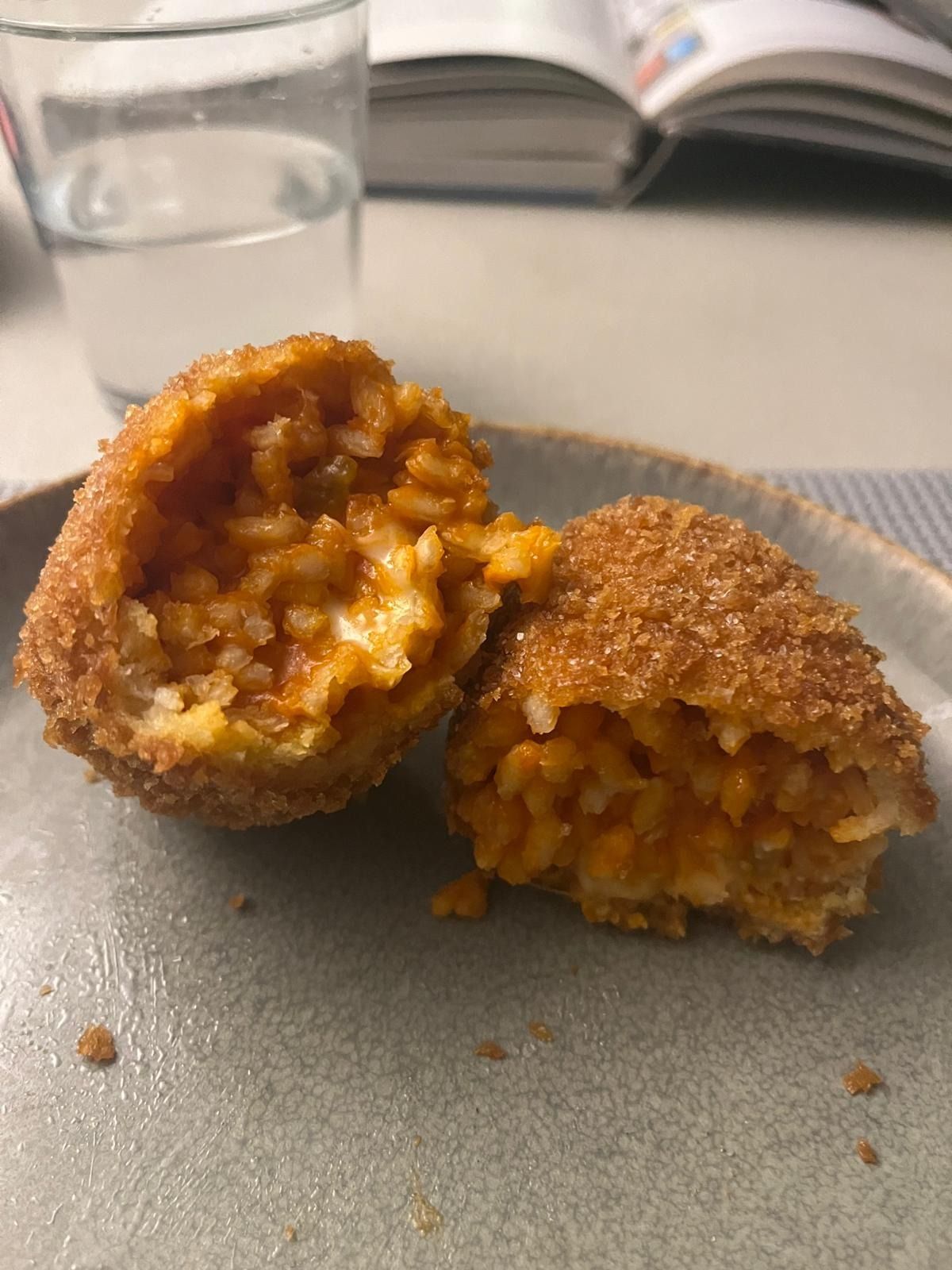 A supplì broken in two, rice in tomato sauce inside a crisp breadcrumb crust, on a grey plate