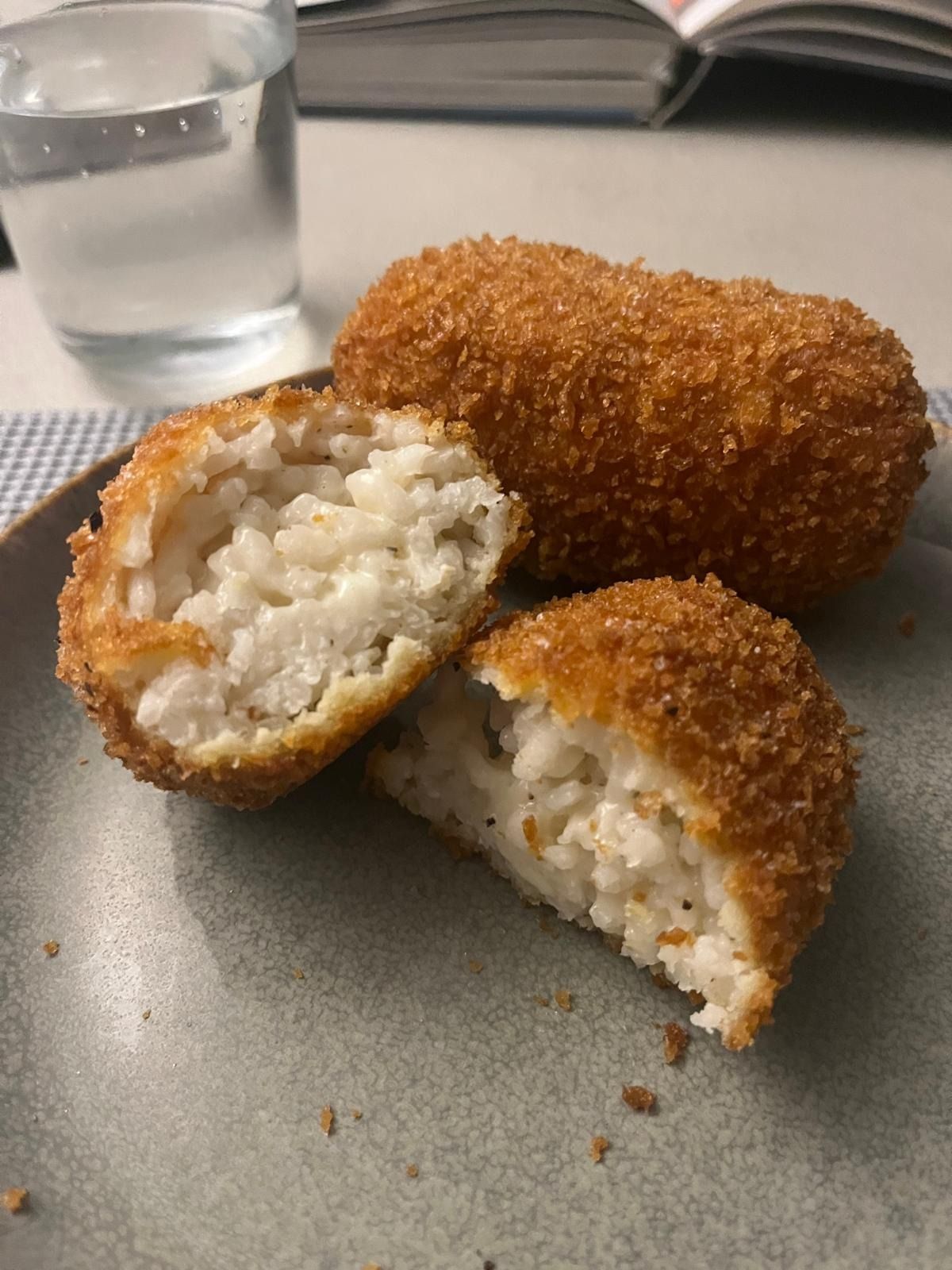 Cacio e pepe supplì broken open, white rice flecked with black pepper inside a golden crust, on a grey plate