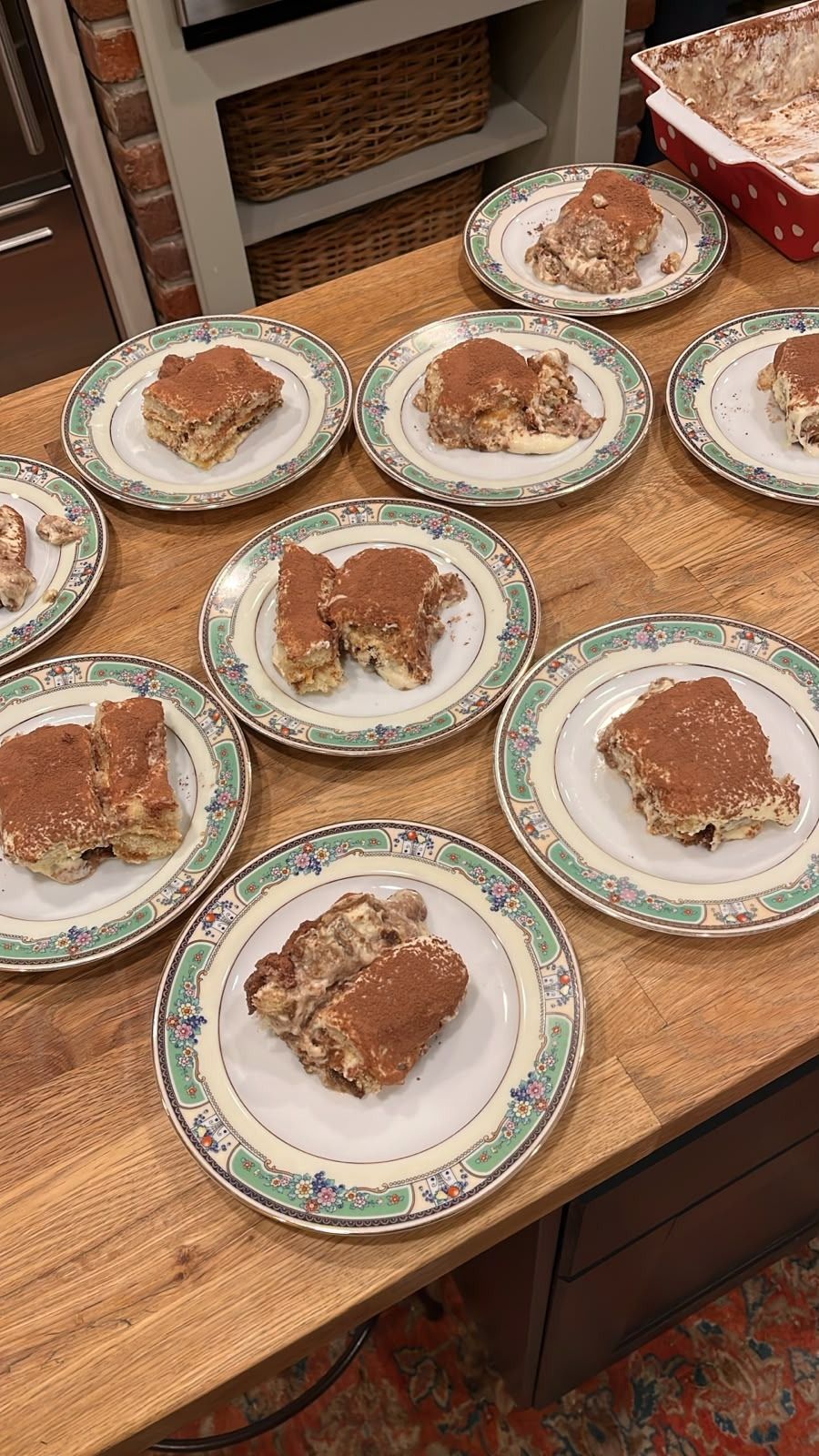 Portions of tiramisù dusted with cocoa on patterned plates, set out on a wooden counter